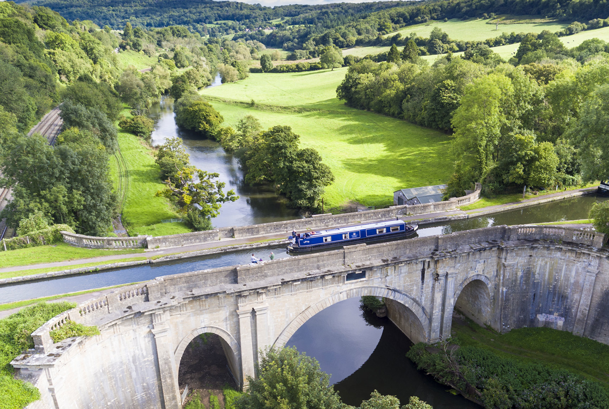 blue canal boat crossing river by aqueduct