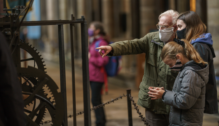 Family wearing masks looking at old mechanical clock in Salisbury Cathedral.